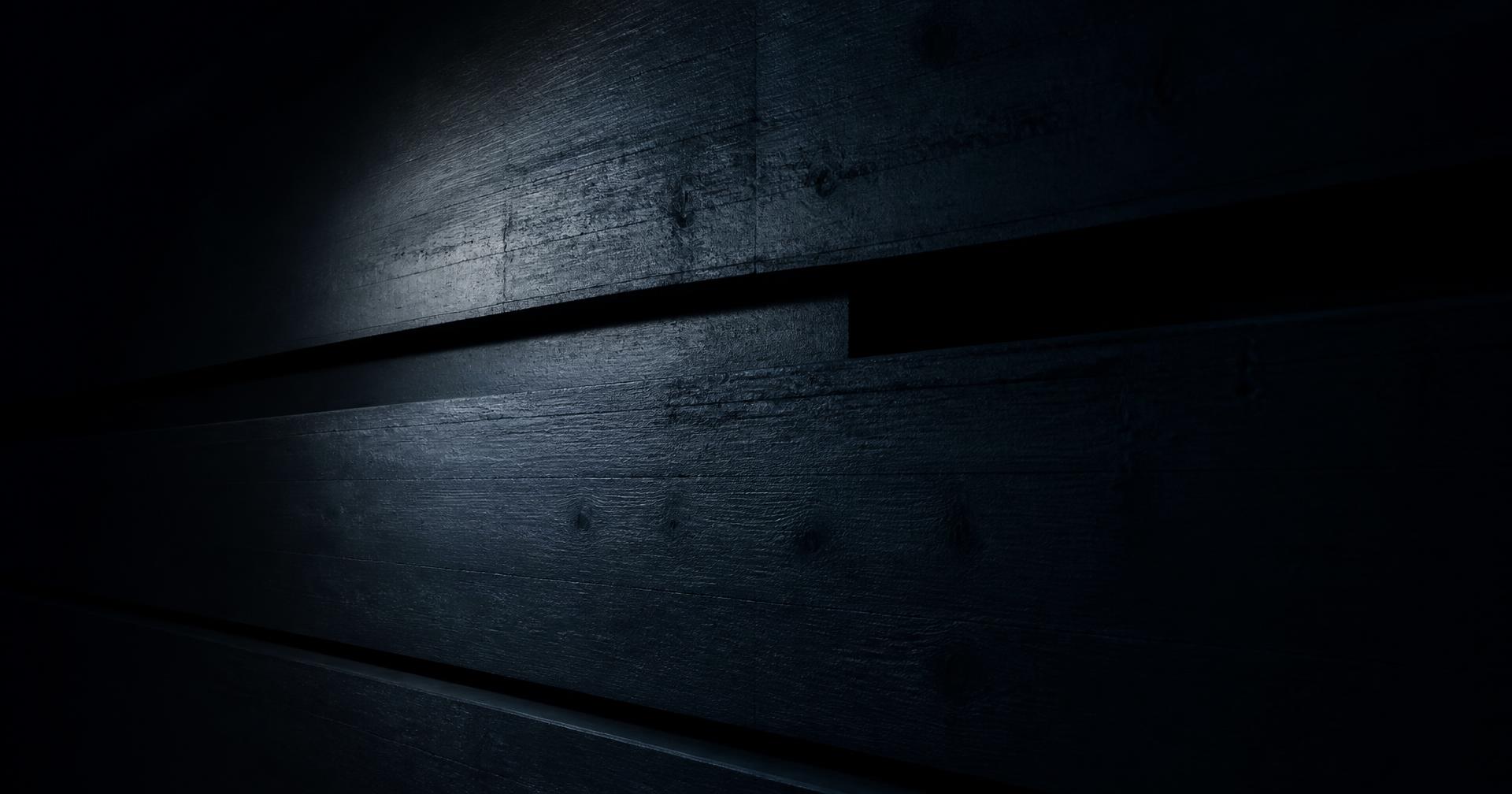Dark board-formed concrete wall with slim shadow gaps lit by a single grazing light