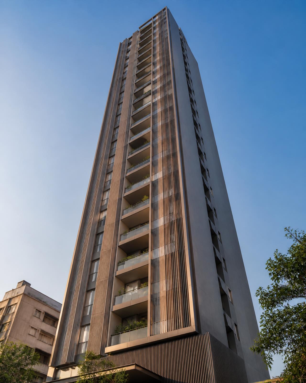 Upward view of a slim modern residential tower with vertical fins and stacked balconies against a clear sky