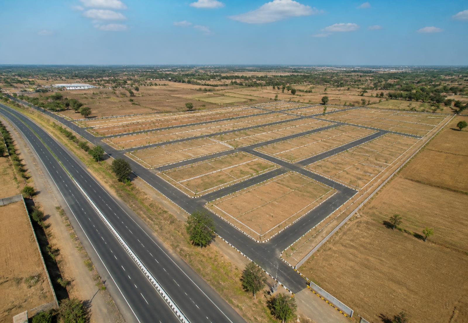 Aerial view of a newly laid plotted township with fresh internal roads beside a rural highway