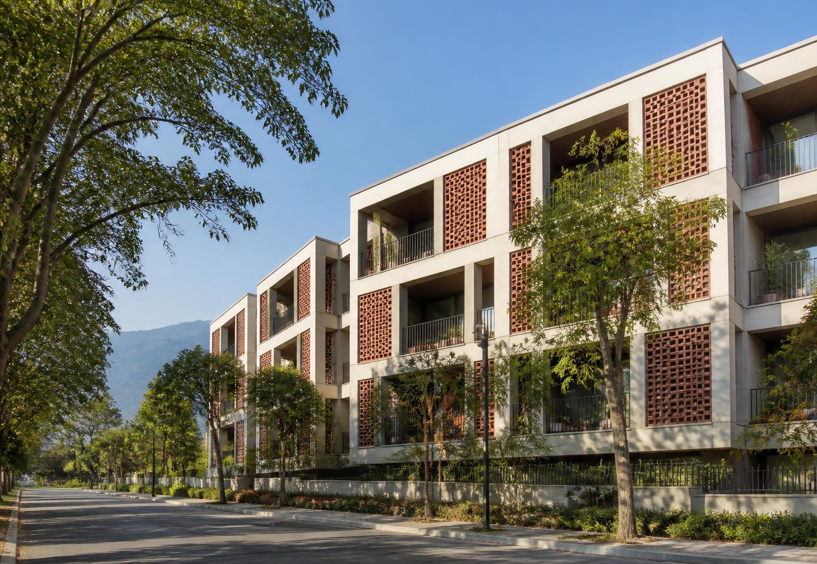 Low-rise apartment building with terracotta screen panels and deep balconies on a tree-lined road with hills behind